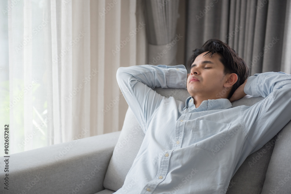 Young asian man sitting on comfortable couch in the living room at home and having a rest from a work with closed eyes. Calm peaceful guy enjoying quiet time alone in the room and dreaming. Young asian man sitting on comfortable couch in the living room at home and having a rest from a work with closed eyes. Calm peaceful guy enjoying quiet time alone in the room and dreaming.