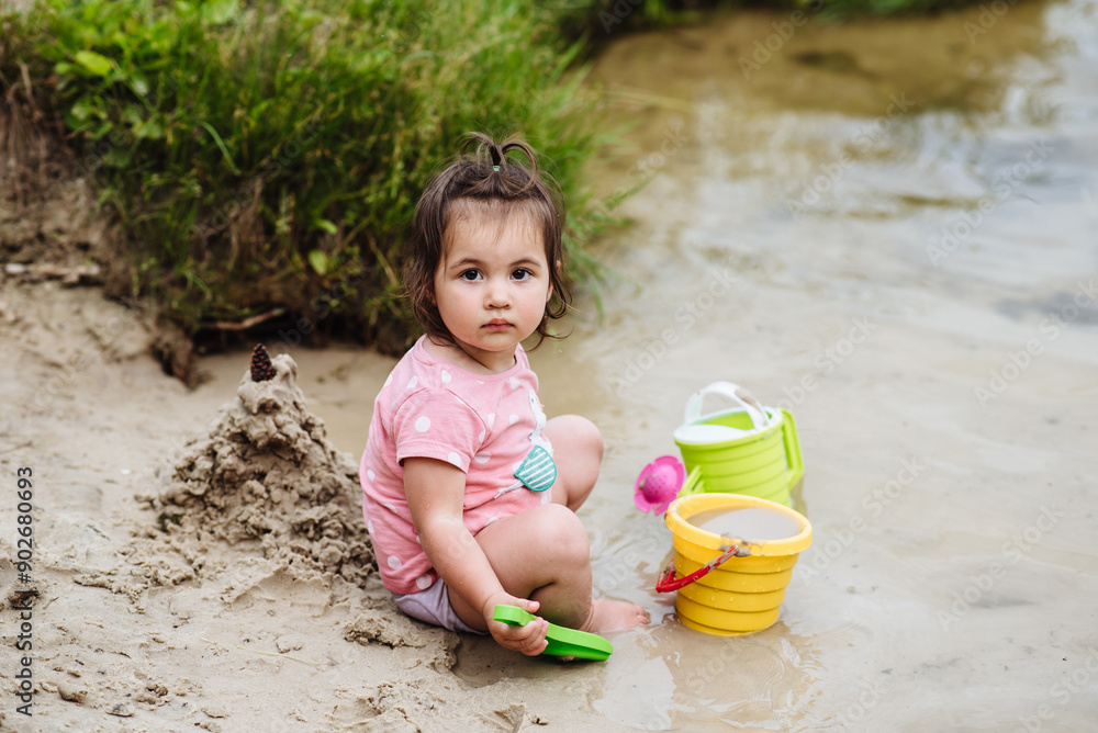 Cute little girl builds a sand castle on the beach. The child plays in the sand Cute little girl builds a sand castle on the beach. The child plays in the sand