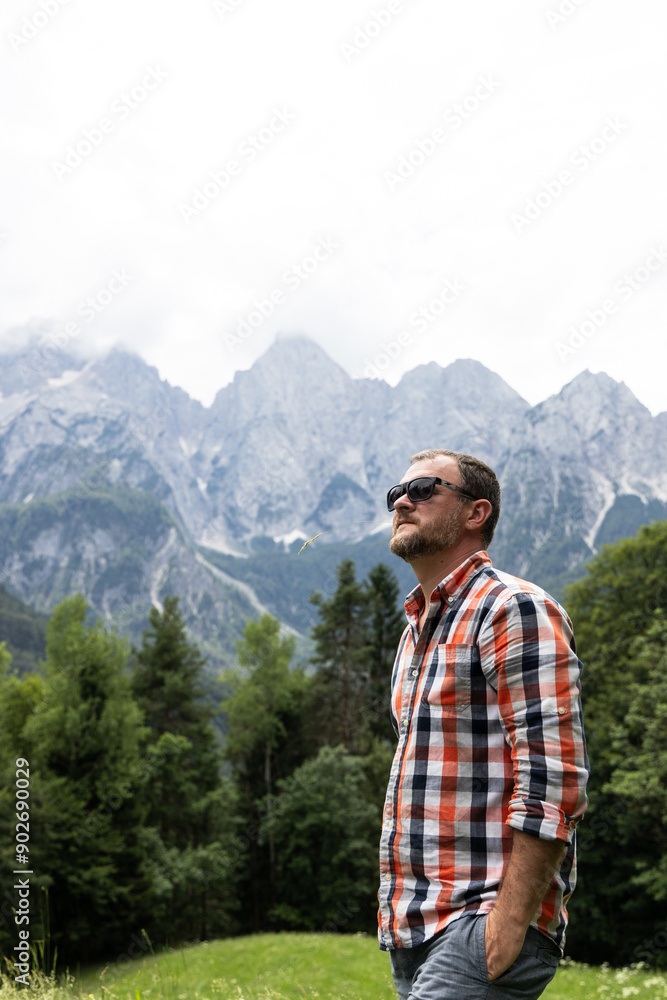 male tourist in a plaid shirt and sunglasses standing against the backdrop of the majestic Mount Triglav in Slovenia. He looks into the distance, enjoying the view of the picturesque mountains, emphas male tourist in a plaid shirt and sunglasses standing against the backdrop of the majestic Mount Triglav in Slovenia. He looks into the distance, enjoying the view of the picturesque mountains, emphas