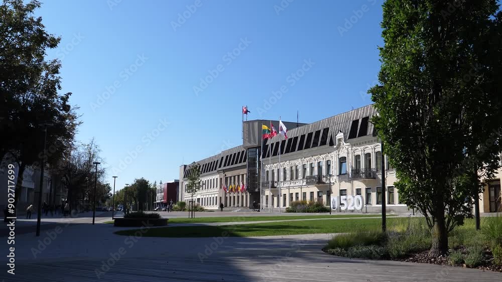Panevezys city downtown square, on the right - town hall decorated with flags, blurry distant people. Panevezys city downtown square, on the right - town hall decorated with flags, blurry distant people.
