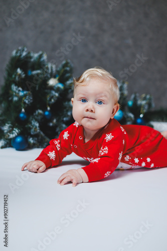 The baby lies near the Christmas tree Children's first Christmas. A little child is celebrating Christmas. New Year holidays. Child with Santa tree. Santa baby.