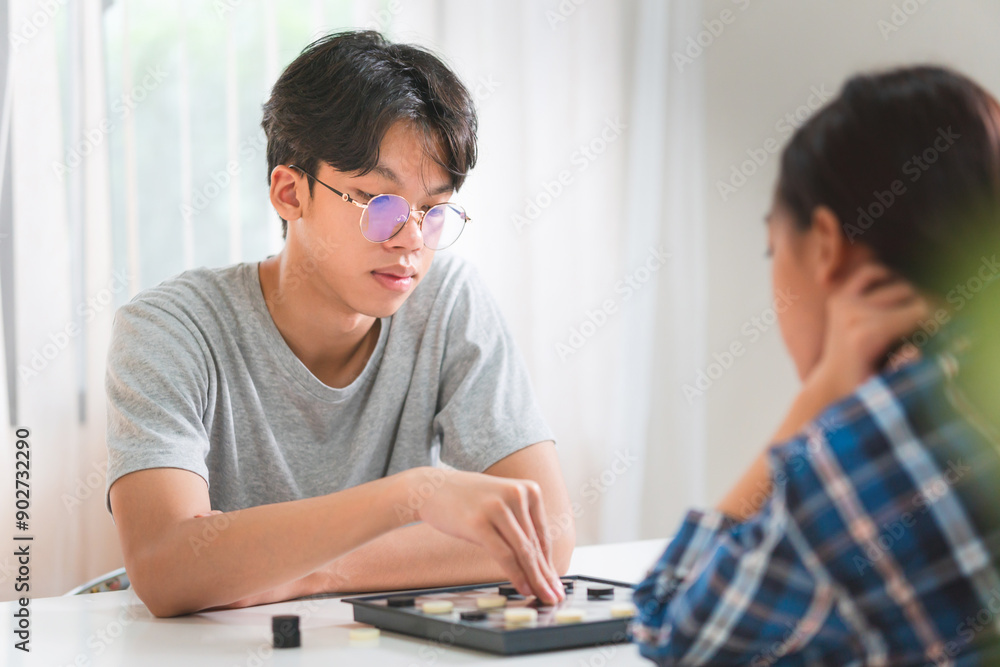 Asian teenage girl and boy playing board game, Asian brother and sister relaxing hobbies playing a game of checkers in living room Asian teenage girl and boy playing board game, Asian brother and sister relaxing hobbies playing a game of checkers in living room