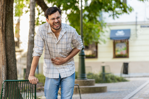 Arabian young man traveler feeling sudden strong abdominal stomach ache, gastritis problem. Upset tourist guy having symptom poisoning diarrhea indigestion peptic ulcer pancreatitis on city street.