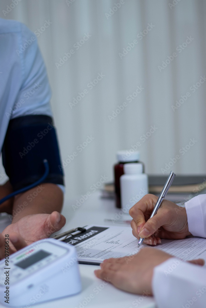 Fototapeta premium A beautiful Asian female doctor is measuring a patient's blood pressure and listening to his heartbeat. Ayoung man who came to see a doctor at a hospital.
