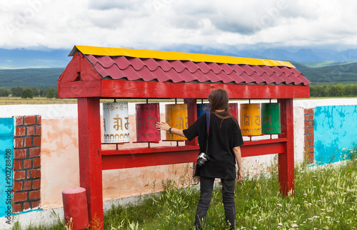 Tourist girl spins prayer drums near Buddhist stupa of on summer day. Siberia. Baikal region. Tunka foothill valley. Galbay village photo