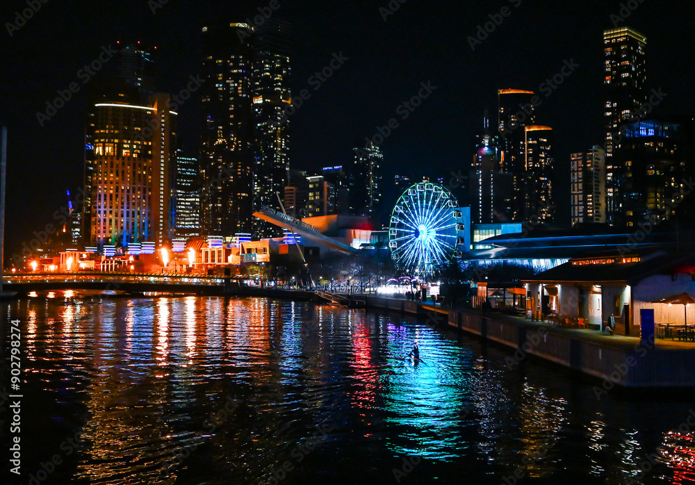 Fototapeta premium A person paddles in a Kayak down the Yarra River, Melbourne, Australia at night in front of the Melbourne CBD