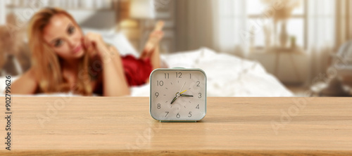 An alarm clock on wooden countertop with copy space. Blurred cozy atmosperic and nostalgic bedroom background with a young woman in bed. photo