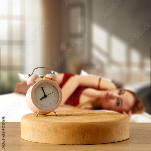 An alarm clock on wooden countertop with copy space. Blurred cozy atmosperic and nostalgic bedroom background with a young woman in bed. photo