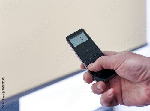 Remote control for window blinds. Man holds in his hand black remote control panel with display and operate motorized roller shades. Radio control electric blinds close-up.