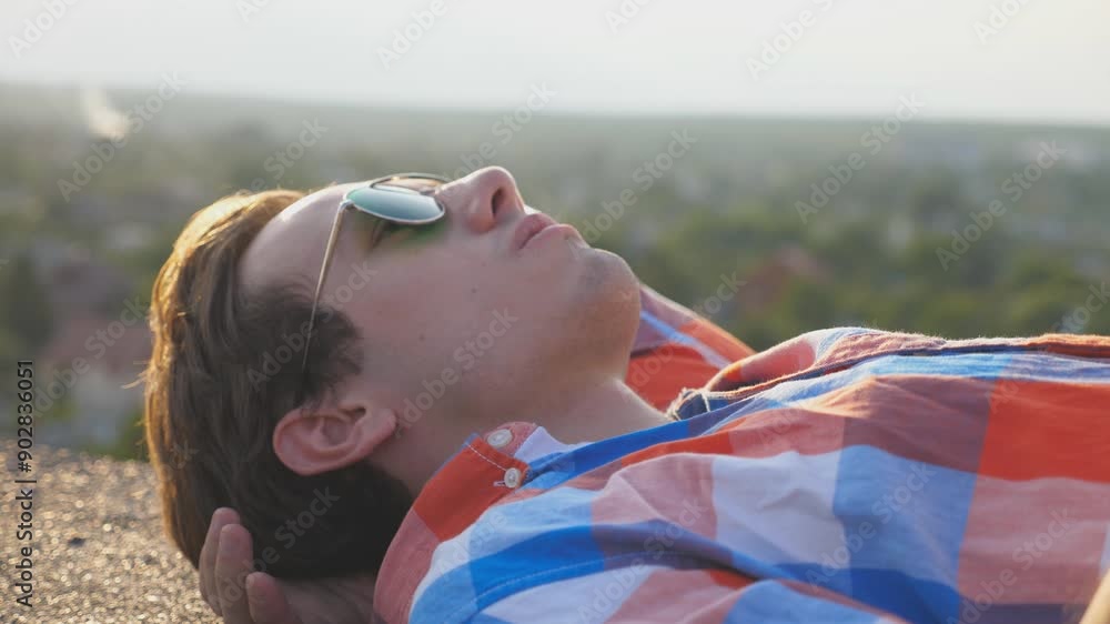 Young man in sunglasses lying of the edge on rooftop of high-rise ...
