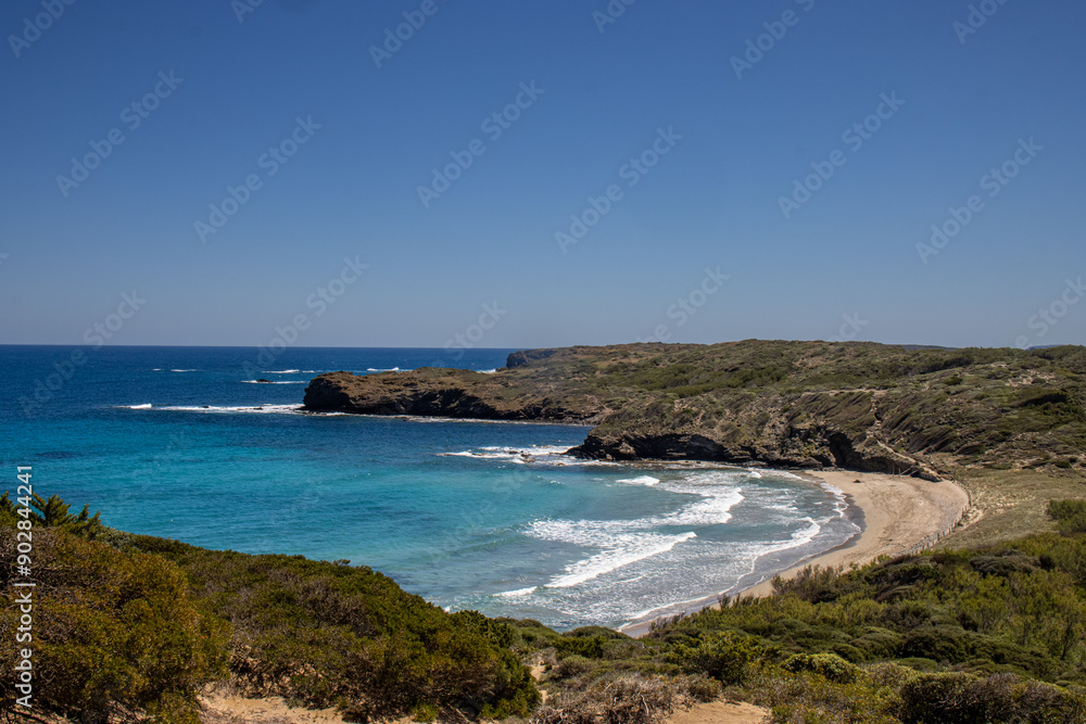 Tortuga beach, a pristine beach with golden sand and crystal-clear turquoise waters. Surrounded by green hills and rocks, the scene conveys tranquility and natural beauty. Menorca, Spain Tortuga beach, a pristine beach with golden sand and crystal-clear turquoise waters. Surrounded by green hills and rocks, the scene conveys tranquility and natural beauty. Menorca, Spain