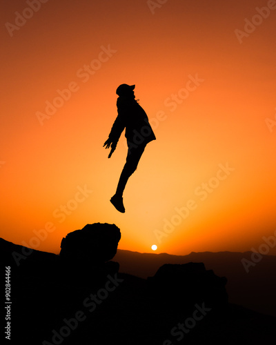 silhouette of a person jumping over a rock 