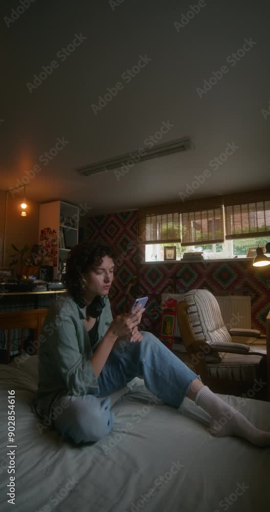 A young woman uses a mobile phone while sitting on a bed at home with a depressed look A young woman uses a mobile phone while sitting on a bed at home with a depressed look