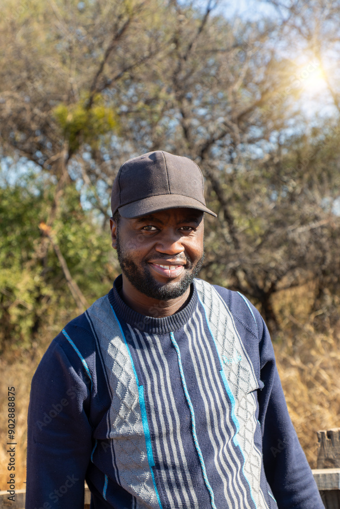 smiling african man with a beard wearing a cap , village sunset, bush in the background smiling african man with a beard wearing a cap , village sunset, bush in the background