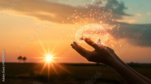 Fototapeta Naklejka Na Ścianę i Meble -  Hand holding a glowing brain shape against a sunset sky.