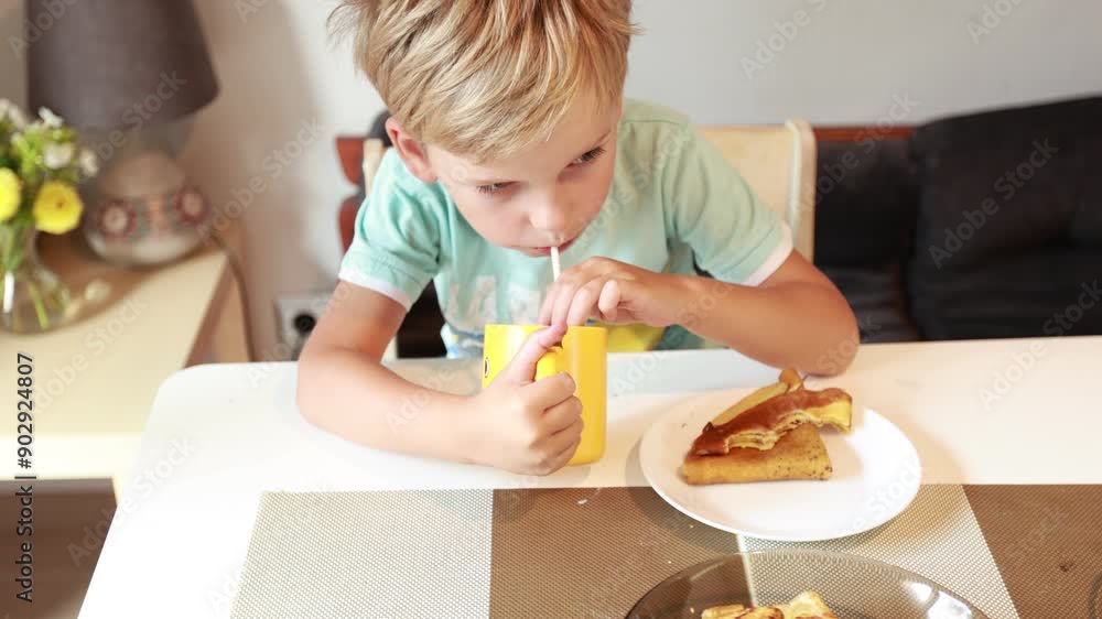 Caucasian Boy Enjoys Snack While Sitting at Kitchen Table During Daytime Caucasian Boy Enjoys Snack While Sitting at Kitchen Table During Daytime