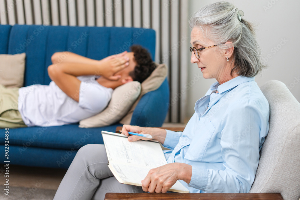 Psychotherapist taking notes while patient lying on couch is covering face Psychotherapist taking notes while patient lying on couch is covering face