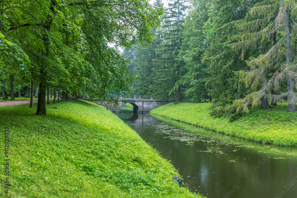 A stone bridge spans a tranquil canal, surrounded by vibrant green foliage and tall trees, creating a peaceful and picturesque scene. A stone bridge spans a tranquil canal, surrounded by vibrant green foliage and tall trees, creating a peaceful and picturesque scene.