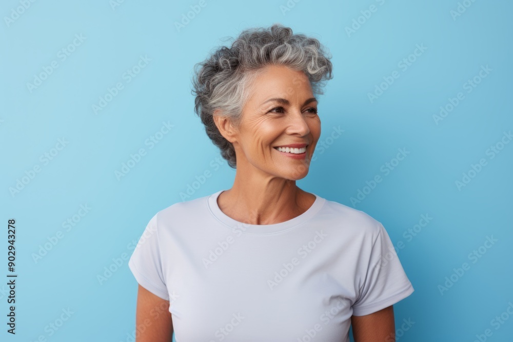 Portrait of a tender woman in her 60s wearing a moisture-wicking running shirt in front of pastel blue background Portrait of a tender woman in her 60s wearing a moisture-wicking running shirt in front of pastel blue background