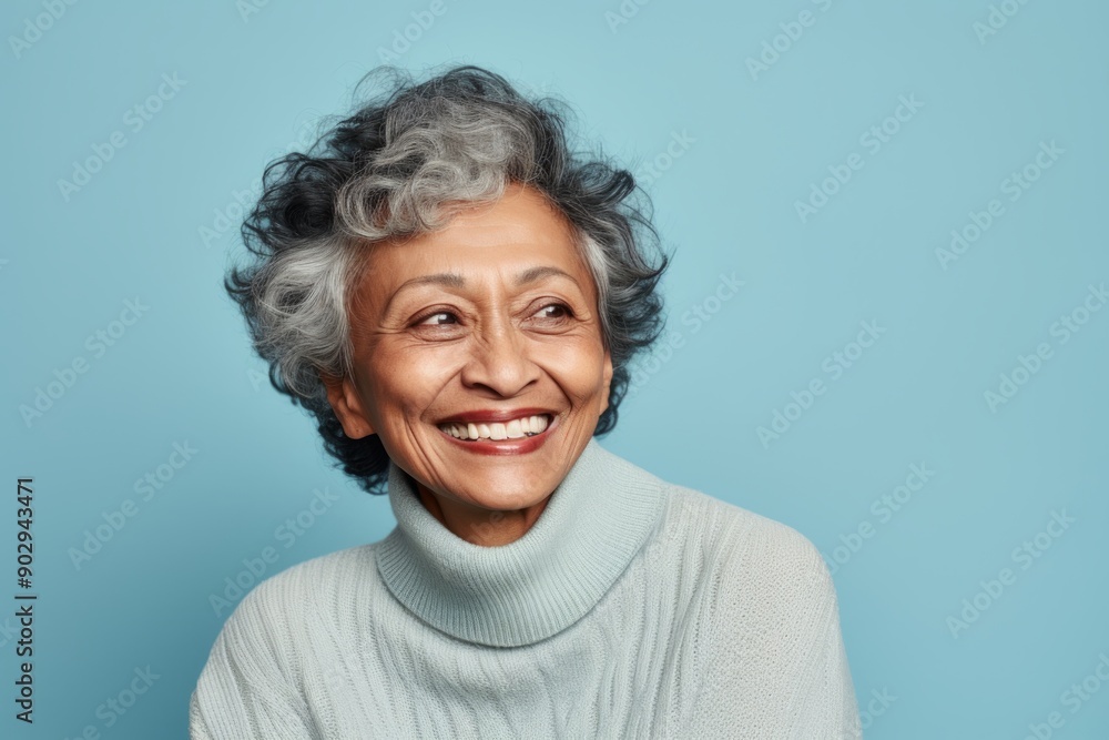 Portrait of a cheerful indian woman in her 80s wearing a cozy sweater while standing against pastel blue background Portrait of a cheerful indian woman in her 80s wearing a cozy sweater while standing against pastel blue background