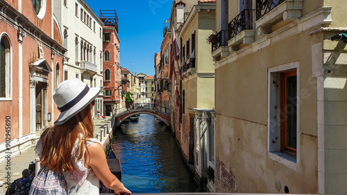 Woman standing on old bridge overlooking the water canals in city of Venice, Veneto, Italy, Europe. Venetian architectural landmarks and old houses facades along the channel. Urban tourism in summer