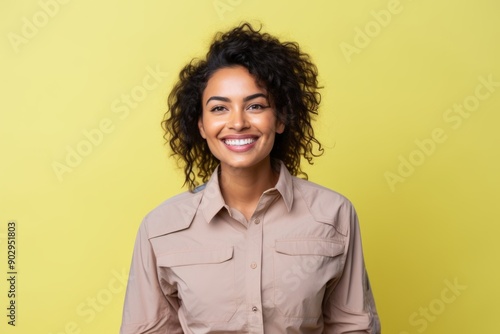 Portrait of a cheerful indian woman in her 20s sporting a breathable hiking shirt in pastel yellow background