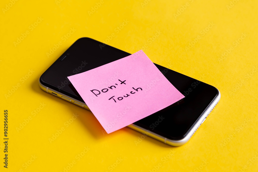 Inscription Don't touch, on a paper reminder on smartphone on a yellow background, digital detox, dependency on tech, no gadget and devices, don't touch personal things. Inscription Don't touch, on a paper reminder on smartphone on a yellow background, digital detox, dependency on tech, no gadget and devices, don't touch personal things.