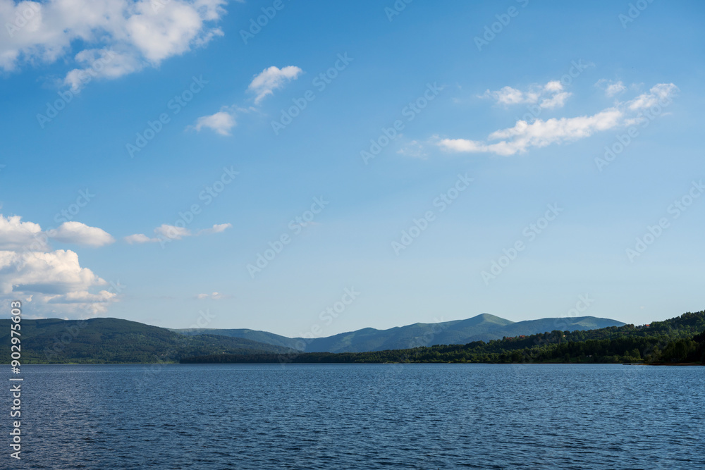 White puffy clouds and blue sky above Vlasina Lake. White cumulus clouds and a blue sky with sun rays. Beautiful semi-artificial lake in Southeast Serbia. White puffy clouds and blue sky above Vlasina Lake. White cumulus clouds and a blue sky with sun rays. Beautiful semi-artificial lake in Southeast Serbia.