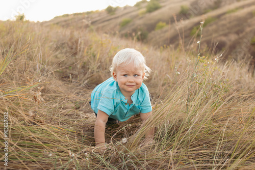 Baby boy with strabismus eyes on nature in summer sitting on grass with sun rays on sunset