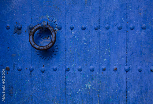 Closeup of old, weathered door painted blue in the Old Town section of Chefchaouen, Morocco, where homes, walls and steps are painted beautiful shades of blue
