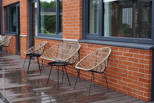 Two beige lounge chairs and sofa. Black metal small tables. Red brick wall on the back. Wet deck after rain. Near Oru hotel. Tallinn, Estonia, Europe. July 2024 photo