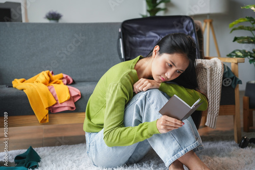 Young woman is feeling down as she reads a letter, surrounded by unpacked belongings in her new apartment photo