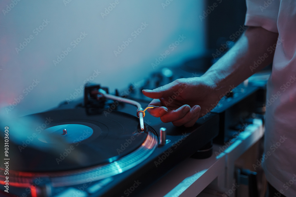 Close-up of a DJ's hand on a turntable, setting up for a music session. Close-up of a DJ's hand on a turntable, setting up for a music session.