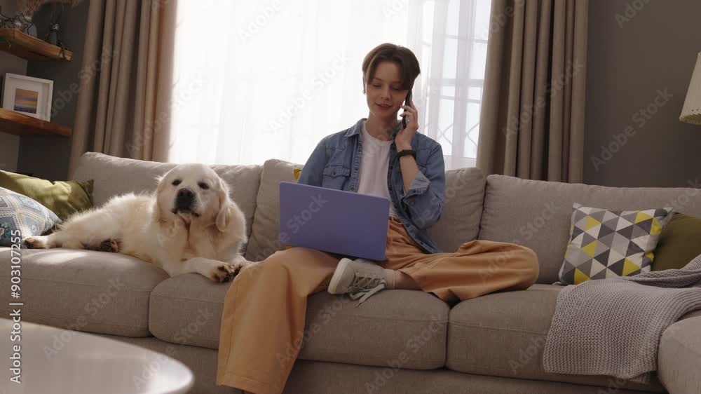 Young Professional Working on Laptop and Talking on Phone While Golden Retriever Resting in Cozy Living Room Young Professional Working on Laptop and Talking on Phone While Golden Retriever Resting in Cozy Living Room