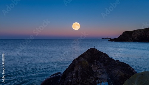 Full moon setting through the rocking just off Holywell Bay, Newquay, Cornwall, UK photo