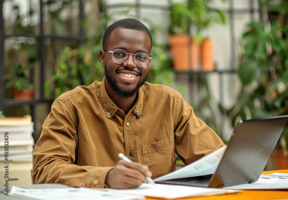 Happy young businessman working on his laptop at his desk in a modern office Happy young businessman working on his laptop at his desk in a modern office