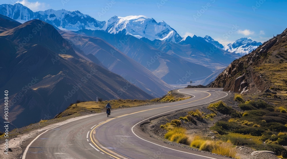 Naklejka premium Winding mountain road ina Valley, California with snow-capped mountains and golden rocks on the sides. mountain range with snow capped mountains in the distance and a cloudy sky.