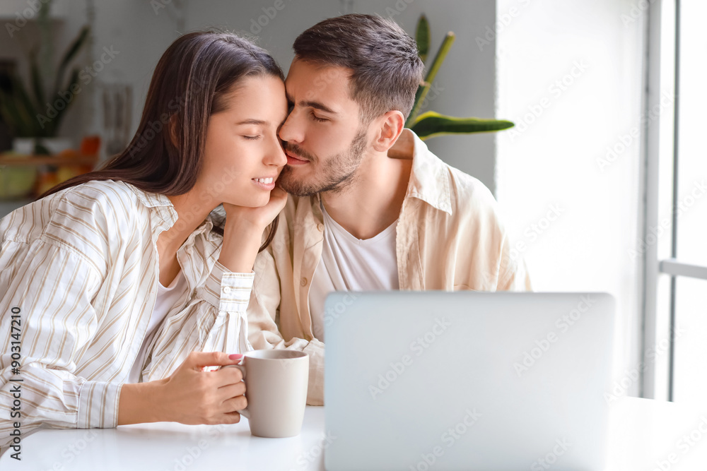 Happy young couple with laptop drinking tea in kitchen