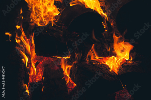 Captivating flames dance in the dark, emitting a warm glow and showcasing the raw power and intense heat of burning wood in a campfire.