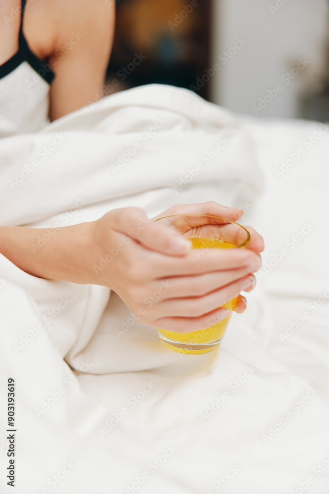 Woman holding cup of orange juice in bed with white sheets and comforter on top Woman holding cup of orange juice in bed with white sheets and comforter on top