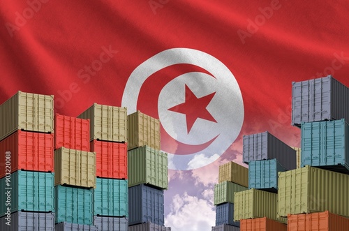 Tunisia flag and big stack of shipping cargo containers in docks with sky background close up