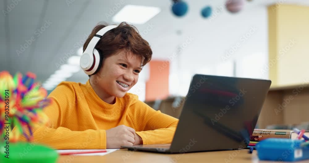 Laughing, school and boy on laptop for online class, remote education or elearning with funny joke. Library, smile or happy male child student listening in headphones on virtual teaching platform Laughing, school and boy on laptop for online class, remote education or elearning with funny joke. Library, smile or happy male child student listening in headphones on virtual teaching platform