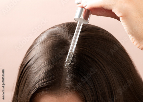 Close up view of unrecognizable young woman putting hair serum for alopecia and hair growth in beige background with selective focus