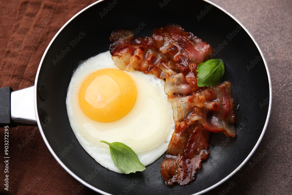 Fried egg, bacon and basil in frying pan on brown table, above view Fried egg, bacon and basil in frying pan on brown table, above view