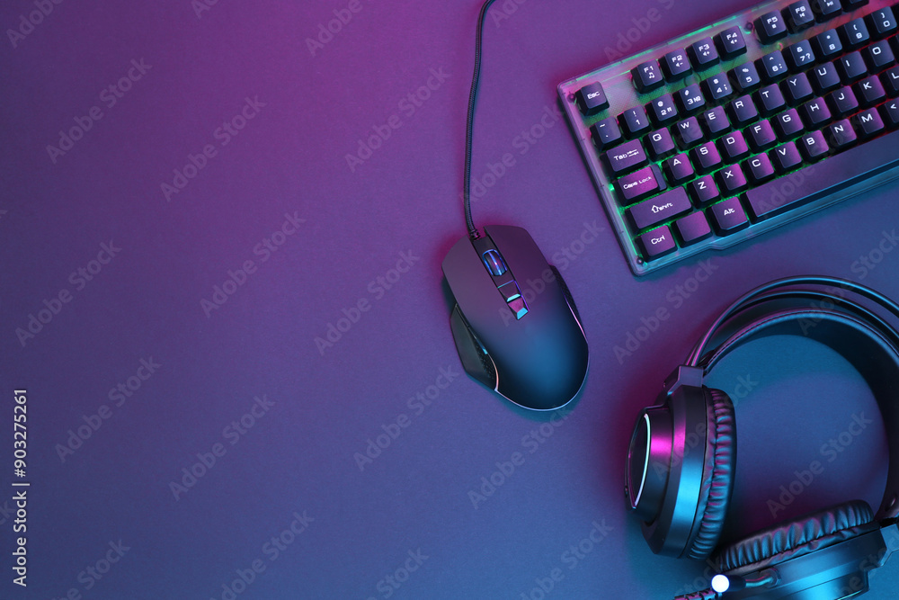 Computer mouse, RGB keyboard and headset in neon lights on dark background, flat lay. Space for text Computer mouse, RGB keyboard and headset in neon lights on dark background, flat lay. Space for text