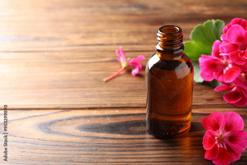 Geranium essential oil in bottle and beautiful flowers on wooden table, space for text Geranium essential oil in bottle and beautiful flowers on wooden table, space for text
