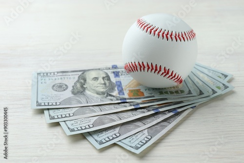 Baseball ball and dollar bills on white wooden table, closeup photo