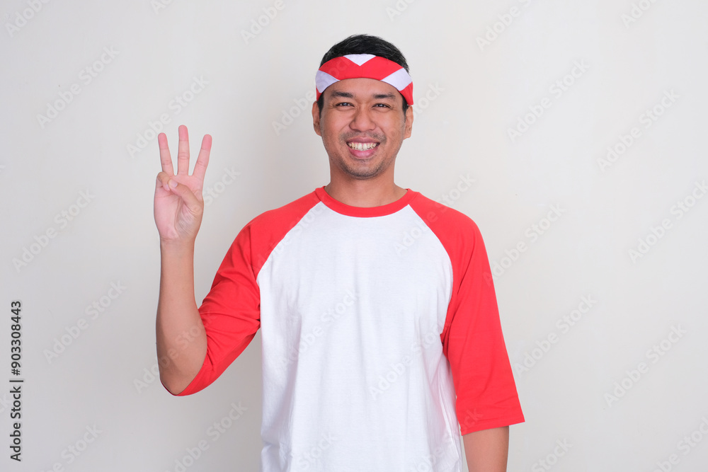 Naklejka premium Adult Asian man smiling at the camera while showing three fingers sign