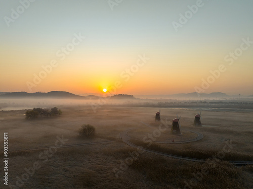 Aerial and sunrise view of trail and windmills with reed and trees on marsh with fog at Sorae Wetland Ecological Park near Incheon, South Korea 