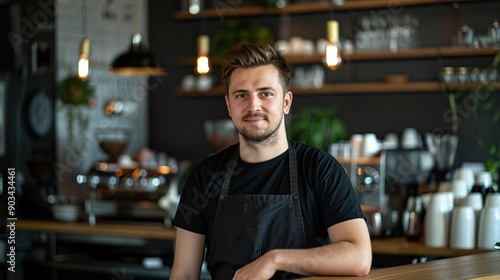 Portrait of a handsome barista in black t-shirt and apron standing at the bar of the modern cafe. copy space. copy space for text.